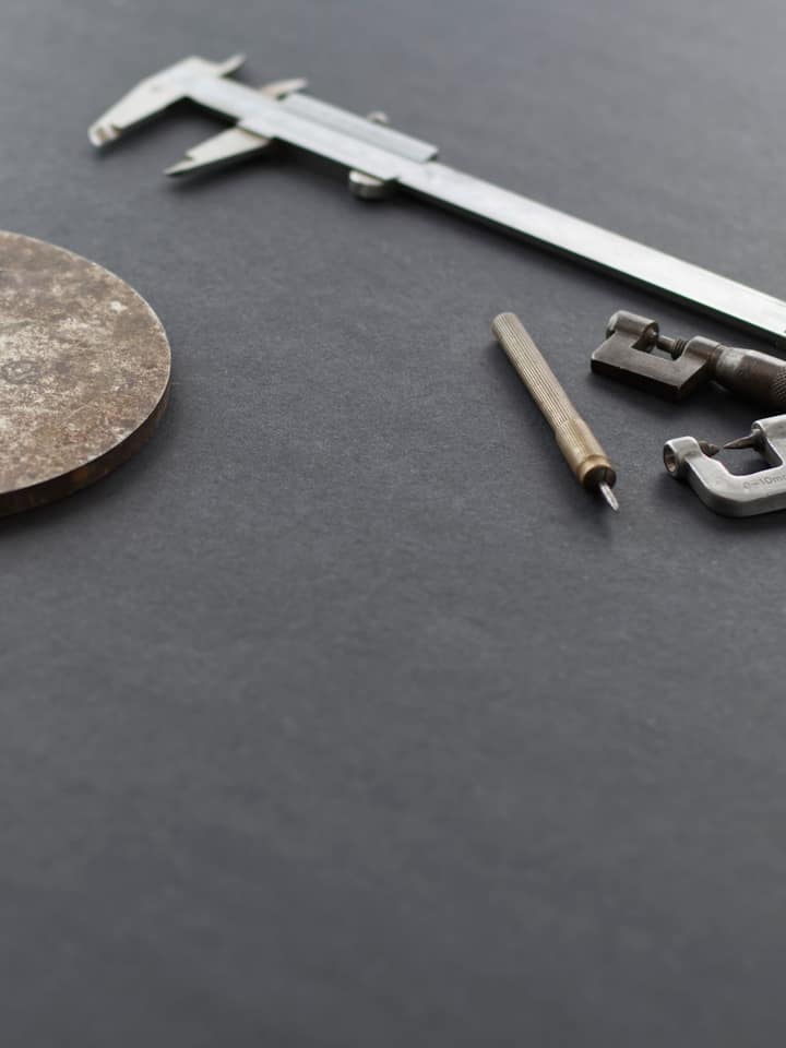 Calipers and a micrometer beside a machined disc on a dark surface