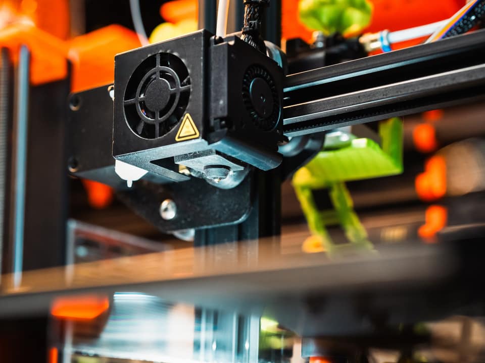 A 3D printer extruder head, printed parts on the plate below it